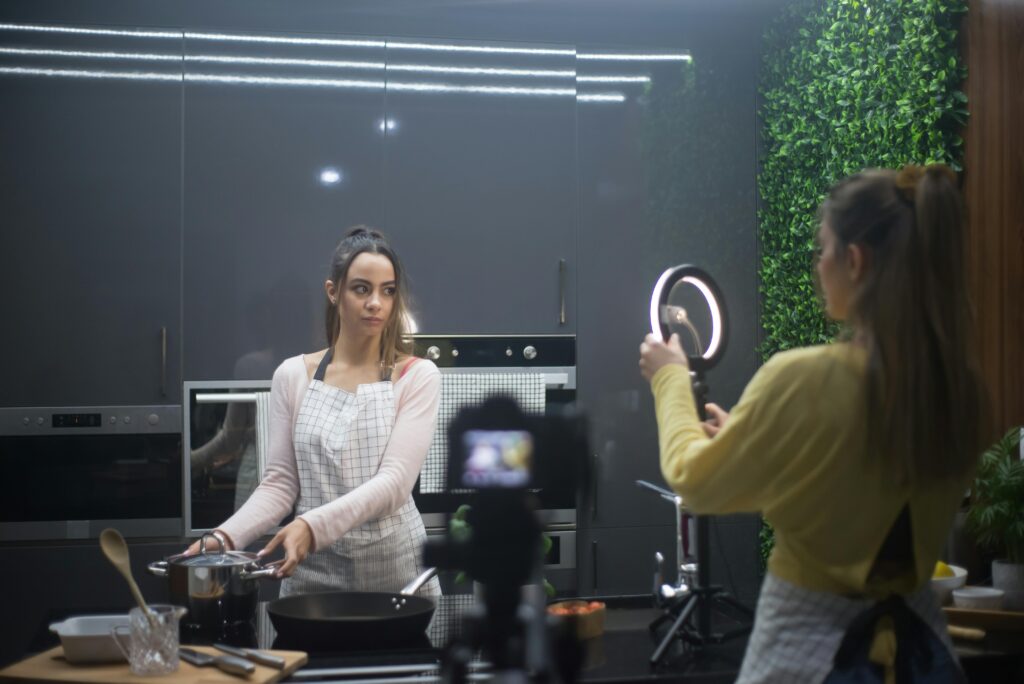 Two women creating a cooking video in a stylish kitchen setup with ring light.